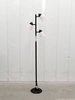 Full view of black metal track tree floor lamp standing against wall