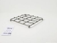 angled view of square metal grid trivet on ball feet