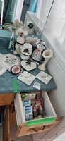 Overall lot on bathroom countertop showing porcelain, crochet figures, cross-stitch, Belleek items