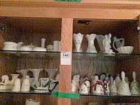 Cabinet shelves showing multiple Belleek shamrock pieces including bells, vases, harp dish