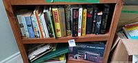 Shelf showing assorted books, boxed Video Cassette Storage Library and loose binder/papers