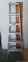 Full front view of aluminum step ladder leaning against wall