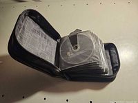 Closed black zippered binder partially opened showing multiple CD sleeves