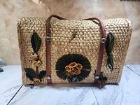 Front view of rectangular wicker picnic basket showing raffia floral decoration and leather straps