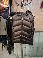 Front view of brown The North Face 550-fill hooded puffer vest hanging on stand