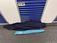 Both umbrellas folded: navy patio umbrella and Margaritaville beach umbrella in blue bag