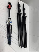 Collapsed MeFOTO tripod beside two collapsed Photobright light stands on white surface