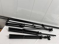 Five black aluminum tripods/poles laid horizontally on table