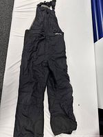 Full view of black Arctix snow bib pants laid flat