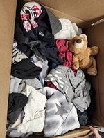 Open cardboard box showing mixed textiles and plush bear