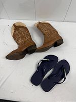Pair of cowboy boots and pair of Havaianas flip flops on table