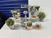 Group shot of seven faux plants and candle stand on table
