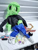 Lot overview showing inflatable alien costume, Wimpy Kid board game, Magic 8 Ball, LED glasses, bag of squishy toys