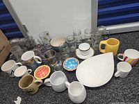 Overview of glass jars, tumblers, mugs, plates and bowl on floor