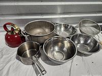 Group shot of all items: red kettle, colander, three mixing bowls, saucepan, mesh strainer