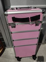 front view of pink rolling makeup trunk showing four chrome-latched compartments, carry handle and wheels