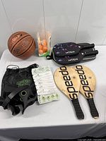 Group shot of all items: basketball, MTEN paddles in cover, Speedo paddles, MonkeyFeet device with bag and instructions, box of ping-pong balls