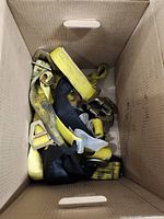 Multiple yellow ratchet straps with metal buckles inside a cardboard box