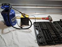 Overview of all four items on white surface: socket set, blue sprayer, yellow heater, sledgehammer