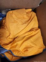 Box containing orange sleeping bag with blue lining