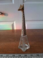 Full view of bottle front showing clear glass base and gold-tone giraffe cap