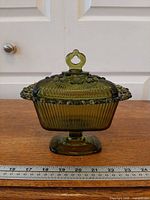Front view of olive green lidded pedestal dish on ruler for scale