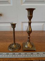 Both brass candlesticks standing side by side with ruler for scale