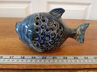 Left side profile of glazed ceramic fish showing perforations and ruler for scale