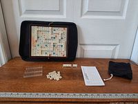 full set laid out including board in folio, racks, tiles, scoring pad, pouch, ruler for scale