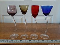 Front view showing four glasses with twisted stems and colored bowls beside ruler
