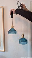 two blue ribbed glass pendant lights held to show size and cords