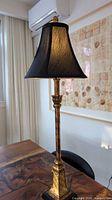 Full view of gold candlestick lamp with black shade on table