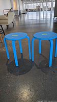two bright blue round four-leg stools side by side on concrete floor