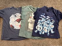 Front view of three Coca-Cola polar bear T-shirts laid flat