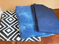 Three folded fabric pieces: black/white geometric, distressed blue, solid navy