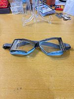 Front view of vintage light blue metal aviator goggles with clear lenses and black strap