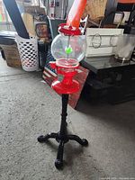 Full view of gumball machine showing red body, glass globe, and black cast iron stand