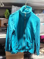 Front view of teal Karen Scott Sport jacket hanging, showing zip, pockets and ribbed trim