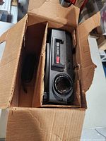 Projector inside original cardboard box showing lens and power cord