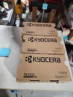 Three Kyocera TK-3122 toner cartridge boxes on table