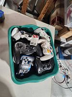 Top view of green tub containing assorted gamepads and RC remotes