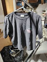 Front view of dark grey tee on hanger showing small chest logo