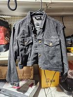 Front of black denim jacket hanging, showing button front, pockets, studs