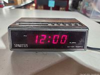 Front view showing red LED display reading 12:00, Spartus logo, alarm and battery reserve labels