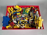 Tray filled with mixed LEGO parts, yellow and blue bricks, windows, wheels, minifigure in center