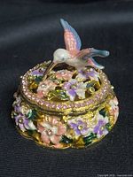 Closed trinket box showing hummingbird, rhinestone band and floral enamel sides
