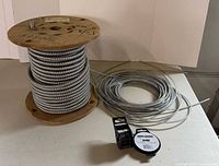 Wooden reel of armored cable, coil of steel cable, solder spool and strapping dispenser visible