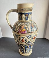 Full frontal view of ceramic pitcher showing relief figures and handle
