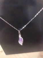 Necklace displayed against black background showing chain and purple stone leaf pendant