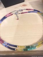 Necklace coiled on wood surface showing multicoloured beads and silver-tone extender